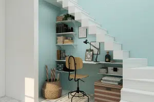 A home office underneath a set of white stairs. 