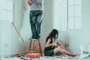 Man and woman painting the walls of their home with newspaper and paint supplies around them.