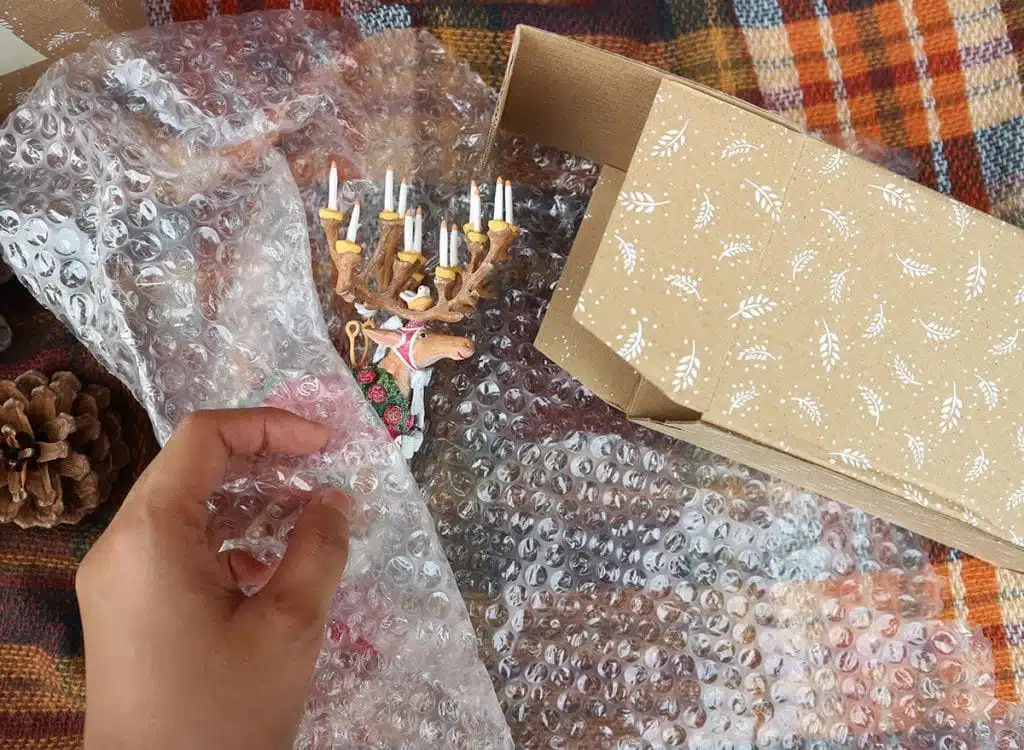 A hand wrapping a fragile tree ornament in bubble wrap and cardboard package